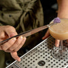 Bartender preparing a cocktail with a skewer and garnish on a bar counter.
