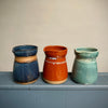 Three ceramic pots in blue, brown, and green on a gray surface with a neutral background