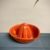 Orange ceramic citrus juicer on a gray surface with a beige background