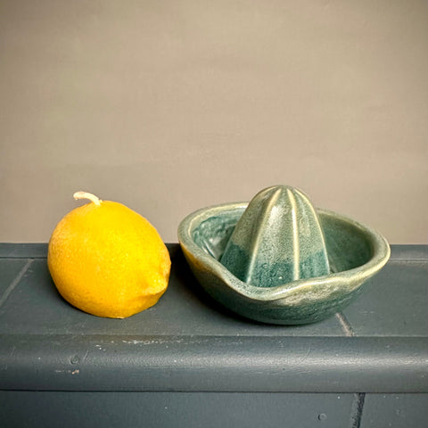 Green ceramic citrus juicer next to a lemon beeswax candle on a gray surface with a beige background