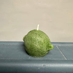 Green candle shaped like a lime on a gray surface with a beige background
