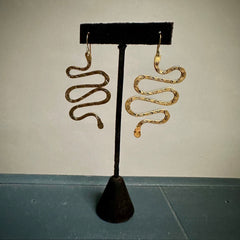 Spiral gold earrings on a black earring stand against a plain background