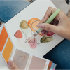 Person holding a color swatch book with a hand holding a green marker.